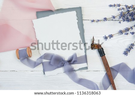 White blank card ribbon bow on a background of pink and blue fabric with lavender flowers and calligraphic pen on a white background. Mockup with envelope and blank card. Flat lay. Top view