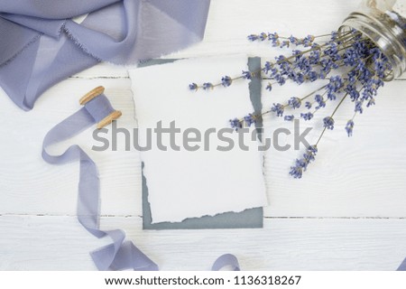 White blank card on a background of blue ribbon with lavender flowers on a white background. Mockup with envelope and blank card. Flat lay. Top view