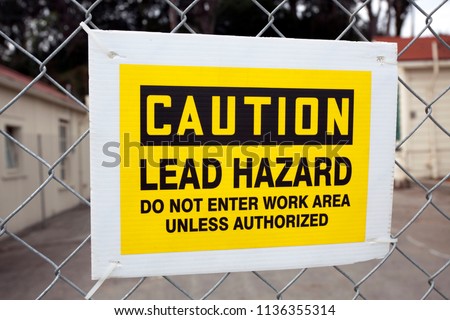 CAUTION LEAD HAZARD sign attached to chain link fence.