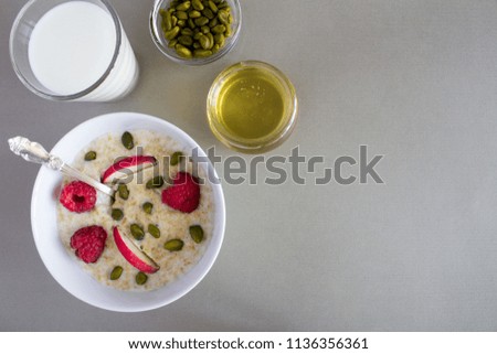 Breakfast: oatmeal with apple,raspberries, honey, nuts and milk in the glass   on the grey  background.Top view.Copy space.