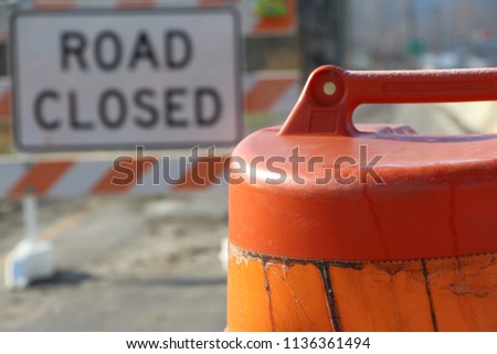 Road closed sign blurred in background of orange barrel