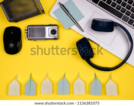 Headphones, laptop, mouse, camera, wallet, pen, notes and paper planes flat view Shot on yellow background