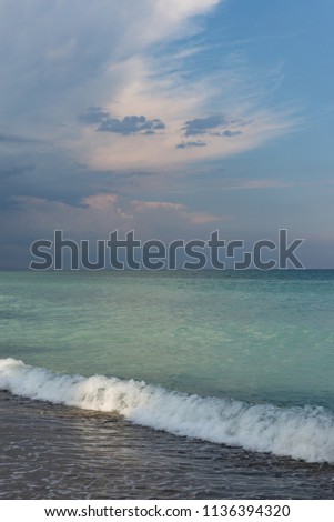 Beautiful seascape with pink clouds on blue sky over turquoise water of the sea surface, attractive pastel light at sunset. Natural combination of colors. Black sea coast, summer tourism in Bulgaria.