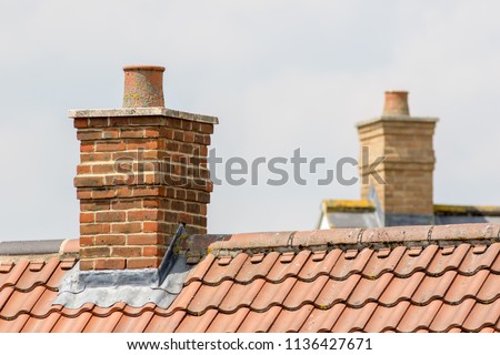 Brick chimney stack on modern contemporary house roof top. Urban housing estate tiled roof in close-up. Royalty-Free Stock Photo #1136427671