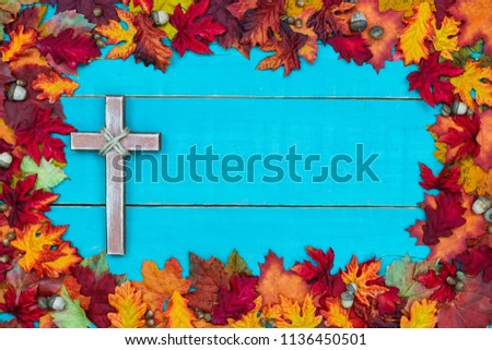 Colorful autumn leaves border with old religious cross hanging on rustic antique teal blue wood background; seasonal religion sign with copy space