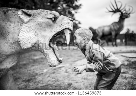 Boy shouting at the artificial saber-toothed tiger Royalty-Free Stock Photo #1136459873