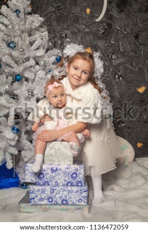 two cute real child sisters pose on a black background with a white Christmas tree together
