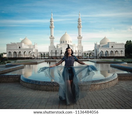 woman in gray dress in front of a white mosque near the pool of water