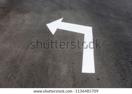 Long white arrow to left. Painted street sign down on asphalt