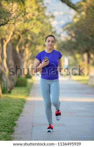 Young woman runner wearing armband and listening to music on earphones. Fit sportswoman taking a break from outdoors training.