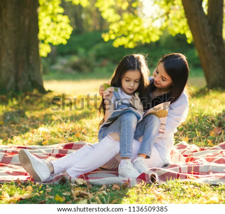 Young latin mother and daughter laughing in city park and read book