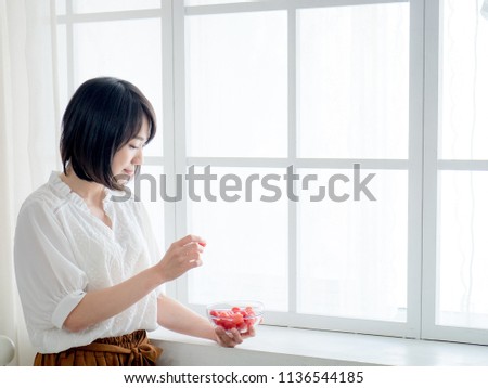 Young woman enjoying tasty healthy fruit in front of window