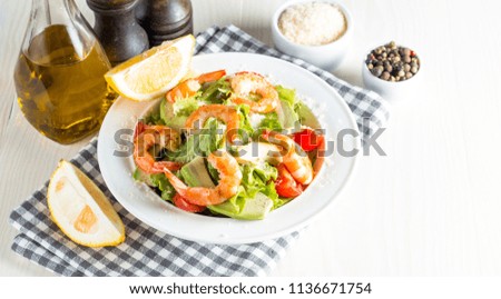 Fresh shrimp salad made of tomato, ruccola, avocado, prawns, chicken breast, arugula, crackers and spices. Caesar salad in a white, transparent bowl on wooden background. Seafood