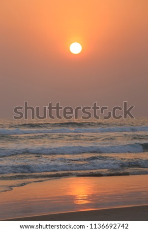Colorful sunset on the atlantic ocean. Picture taken at assinie beach, ivory coast, africa. Seascape with pastel colors. White waves and orange reflects on the wet sand. Calm and quiet ambiance.