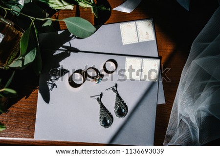 Wedding accessory bride. Stylish earrings, gold rings, flowers, garter on table standing on wooden background. Letters from the bride and groom. flat lay. top view.