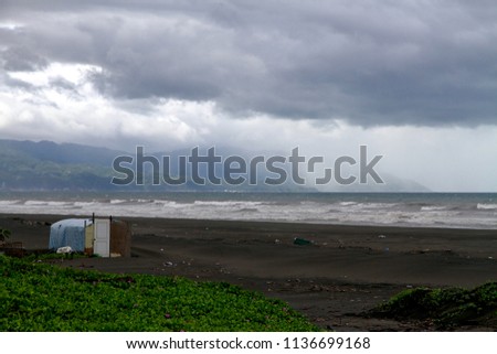 The perspective view of the stormy coastline of Yilan at the North Shore of Lanyang River. The rain on the ocean and mist faraway. The fence on the beach to prevent strong wind.
