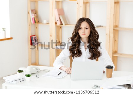 Concentrated young beautiful businesswoman working on laptop in bright modern office