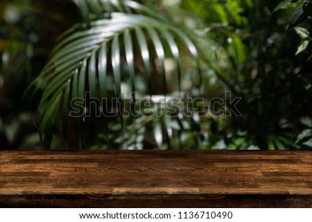 Dark wood table top with blur on green palm leaves or tree in tropical forest with bokeh light at background - Using for Mock up template for display of your design,Banner for advertise of product.