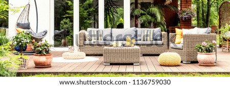 A relaxing spot for a warm, summer day - a stylish, wooden terrace with wicker garden furniture, cushions, plants and flowers Royalty-Free Stock Photo #1136759030