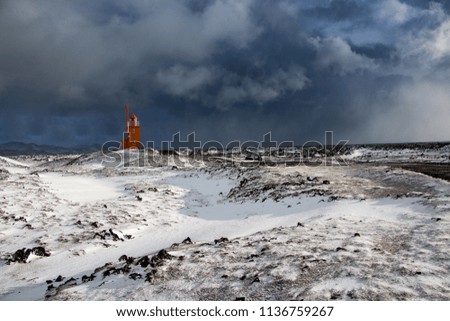 Orange lighthouse on a stony coast in Iceland. Winter landscape