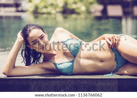 Portrait of young Caucasian woman wearing bikini posing at poolside at summer resort