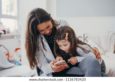 Mom and daughter are looking for something in the smartphone
