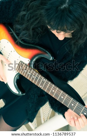 Top view photo of a woman in an elegant dress playing on an electric guitar while standing on a metal stairs.