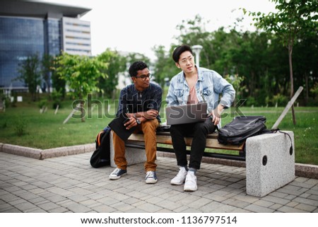 Two young students are discussing a new project. Asian and Indian student. Students live and study on campus. The photo illustrates education, College, school, or University.