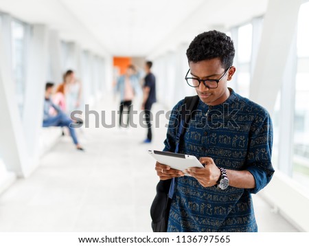 A student from India stands with a tablet at the University. Students in the background. The photo illustrates education, College, school, or University.