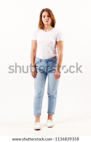 Beautiful girl teenager in white t-shirt and jeans poses in white studio