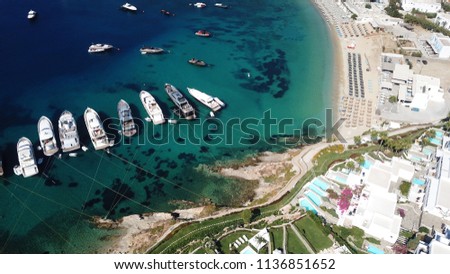 Aerial drone, bird's eye view photo of luxury yachts docked near turquoise sea in paradise beach of Psarou and Platy Gialos full of pool resorts and rocky seascape, Mykonos island, Cyclades, Greece