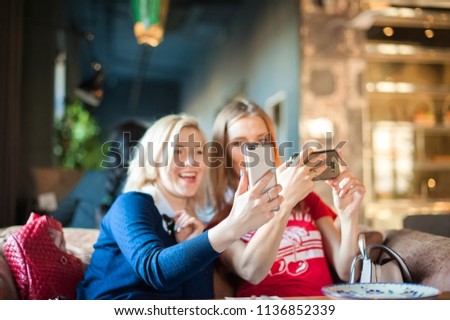 Two young women in a cafe at a table do selfie on phones. Visitors to the restaurant take pictures of themselves on the phone. Focus on phones
