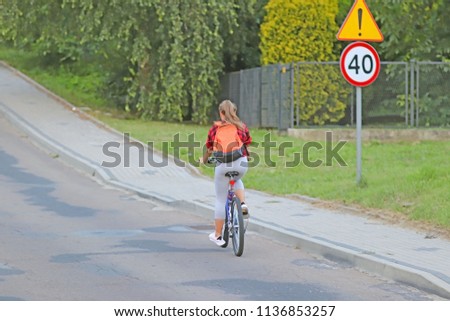 A young girl rides a bicycle on the road by the road sign of danger and speed limits of up to 40 km/h. Active way of life of young people. Ecological mode of transport is popular in the city