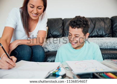 Little boy and his mother are making a Father's Day card at home using crayons and paints.