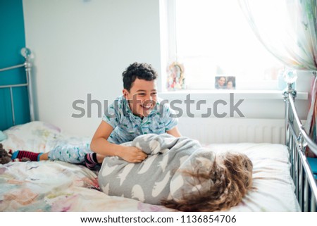 Little boy and his older sister are playfighting on a bed at home.