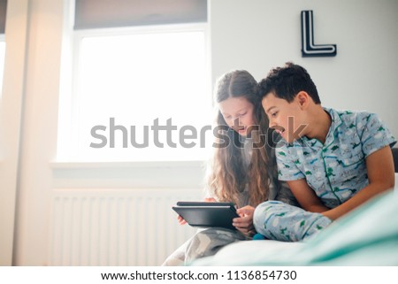 Little girl and her brother are looking at a digital tablet together in the boy's bedroom.