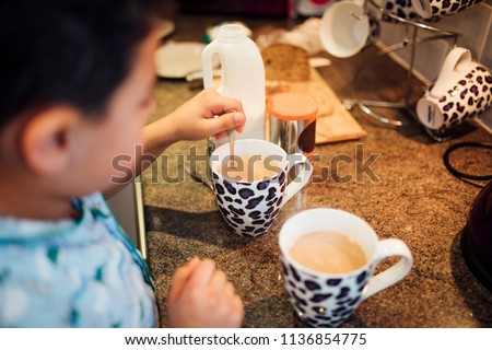 Little boy is helping his dad make tea in the morning. He is mixing the tea with a spoon.