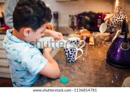 Little boy is pouring milk in to a mug while making tea with his father at home.