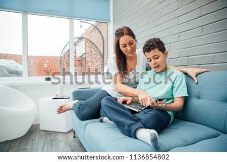 Little boy and his mother are reading a book together in the conservatory of their home.