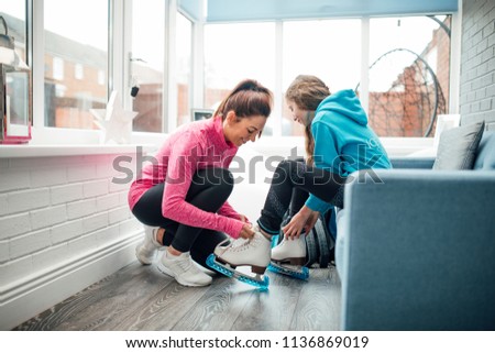Woman is helping her daughter put her figure skates on before she takes her to a skating lesson.