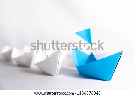 Leadership concept. blue paper ship with flag lead among white. One leader ship leads other ships.