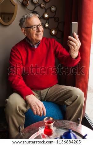 Portrait of senior man who is taking selfie in a cafe. 