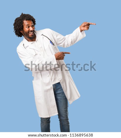 Handsome african american medical doctor pointing to the side, smiling surprised presenting something, natural and casual