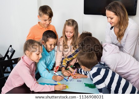 Little cheerful  children with teacher drawing together in classroom