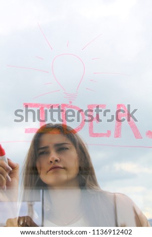 Light bulb idea drown on a window by a cute brunette girl on a cloudy background