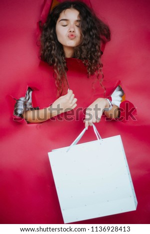 View of girl face through hole in red paper. Cute attractive girl looking through hole. Discount, sale advertising, to insert text or slogan. Discount, sale. Shopping