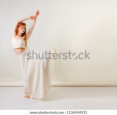 Dancer posing in studio. Young and beautiful redhead girl in a beige long skirt and top dances and poses in studio. Copy space, gray background