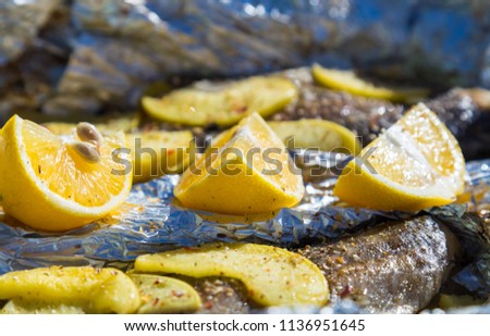 Baked fish in foil with lemon and apples outdoors.