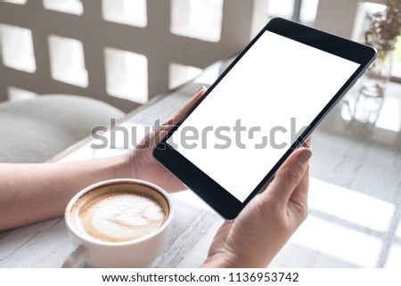 Mockup image of a woman holding black tablet pc with white blank screen with coffee cup on table 