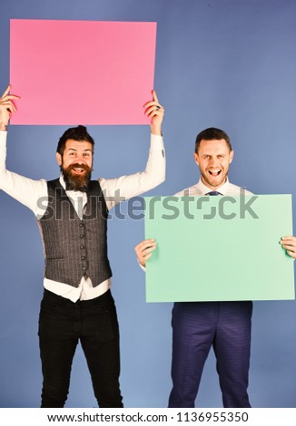 Happy smiling young businessmen showing blank green and pink signboards on blue background. Advertising concept